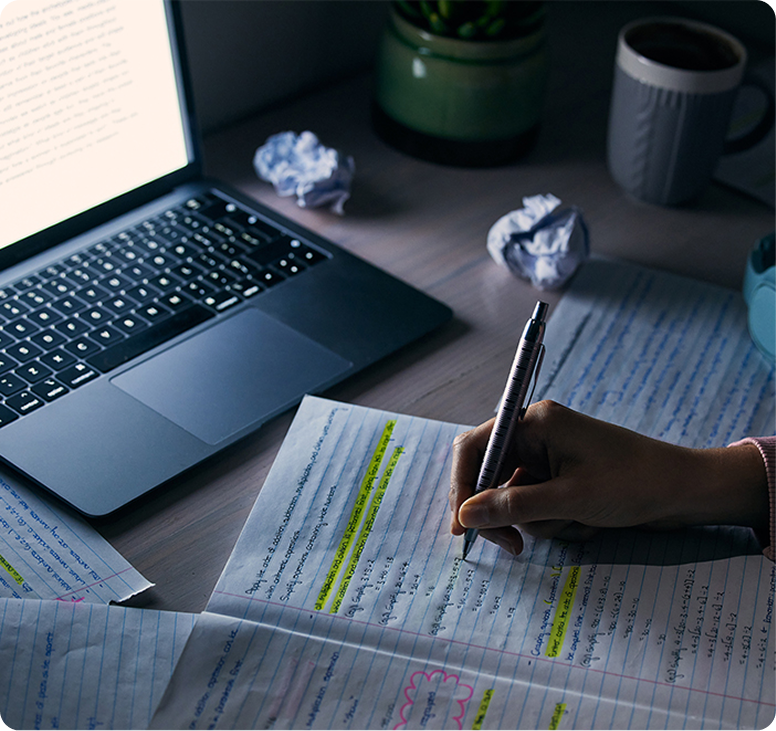Writer drafting handwritten notes next to a laptop and coffee
