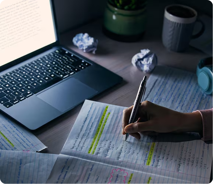 Writer drafting handwritten notes alongside a laptop late at night