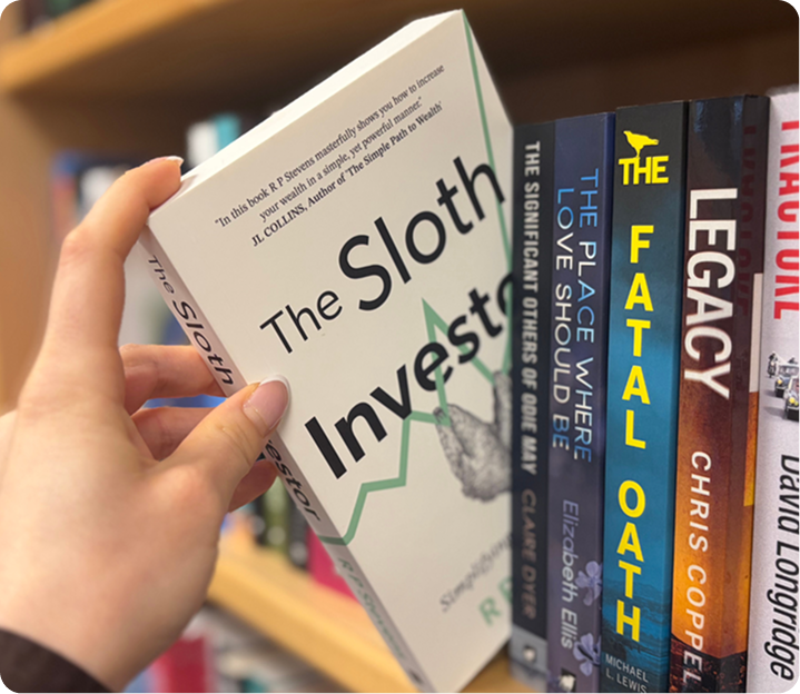 Reader holding a published book in front of a shelf of titles